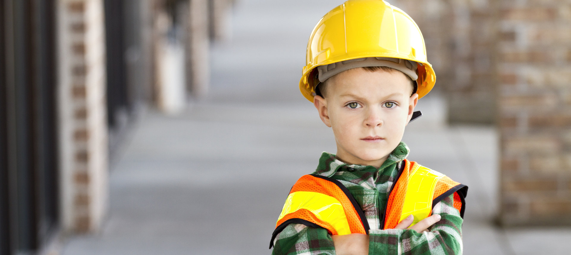 Little Construction Worker Bild von einem kleinen Jungen mit verschränkten Armen. Der junge trägt ein Holzfällerhelm mit Warnweste und einem Bauhelm. Er ist das Symbolbild für unseren Managed IT Security Service.