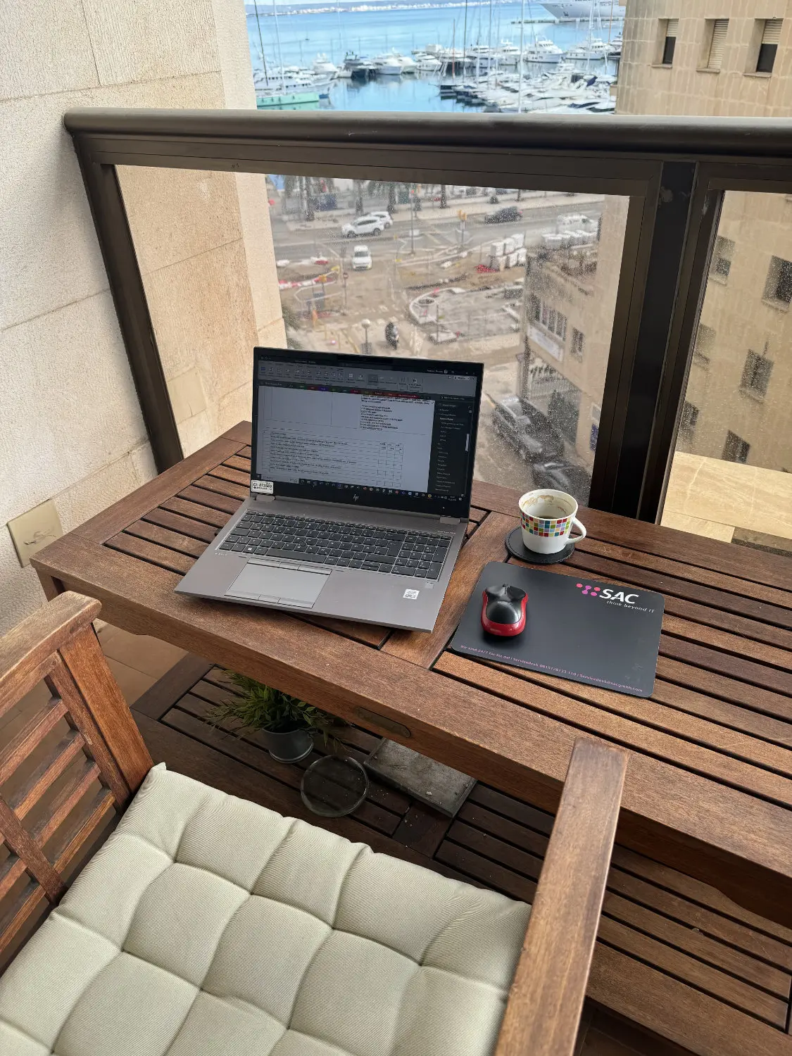 Aufnahme von einem Hotelbalkon mit Aussicht auf den Hafen und das Meer in Palma der Mallorca. Auf einem Tisch steht ein Notebook neben welchem ein Mauspad liegt mit SAC Logo
