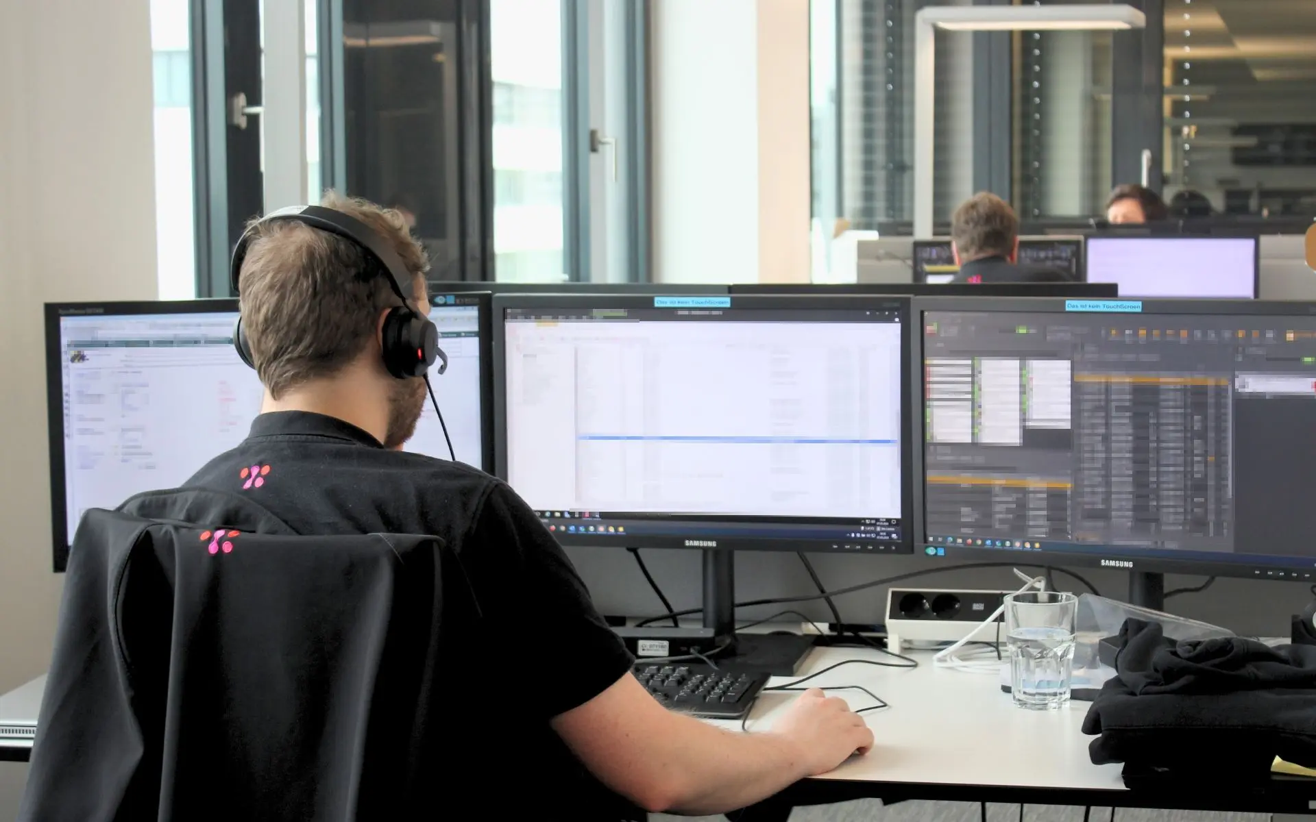 SAC_Foto_User-Supper-Service-Desk Ein SAC Mitarbeiter der an einem Schreibtisch mit mehreren Bildschirmen sitzt und über Headset einem Kunden bei einem IT-Problem hilft.