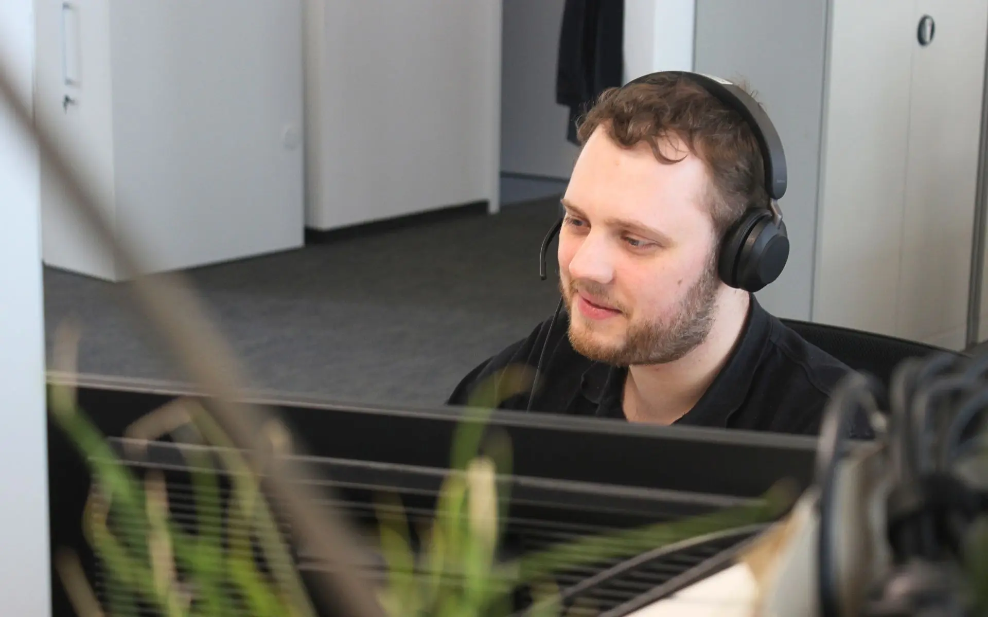 sac_foto_service-desk-mitarbeiter Ein Foto von einem IT-Mitarbeiter. Er arbeitet im IT User Support. Er hilft gerade einem Kunden über remote Support beim lösen eines technischen Problems.